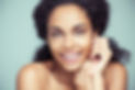 Facial Treatment | A dark-skinned woman looking at the camera and smilng her mouth open while leaning on her hands.  